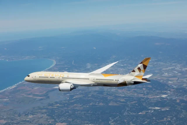 Etihad Airways Boeing 787 Dreamliner flying over a scenic landscape.